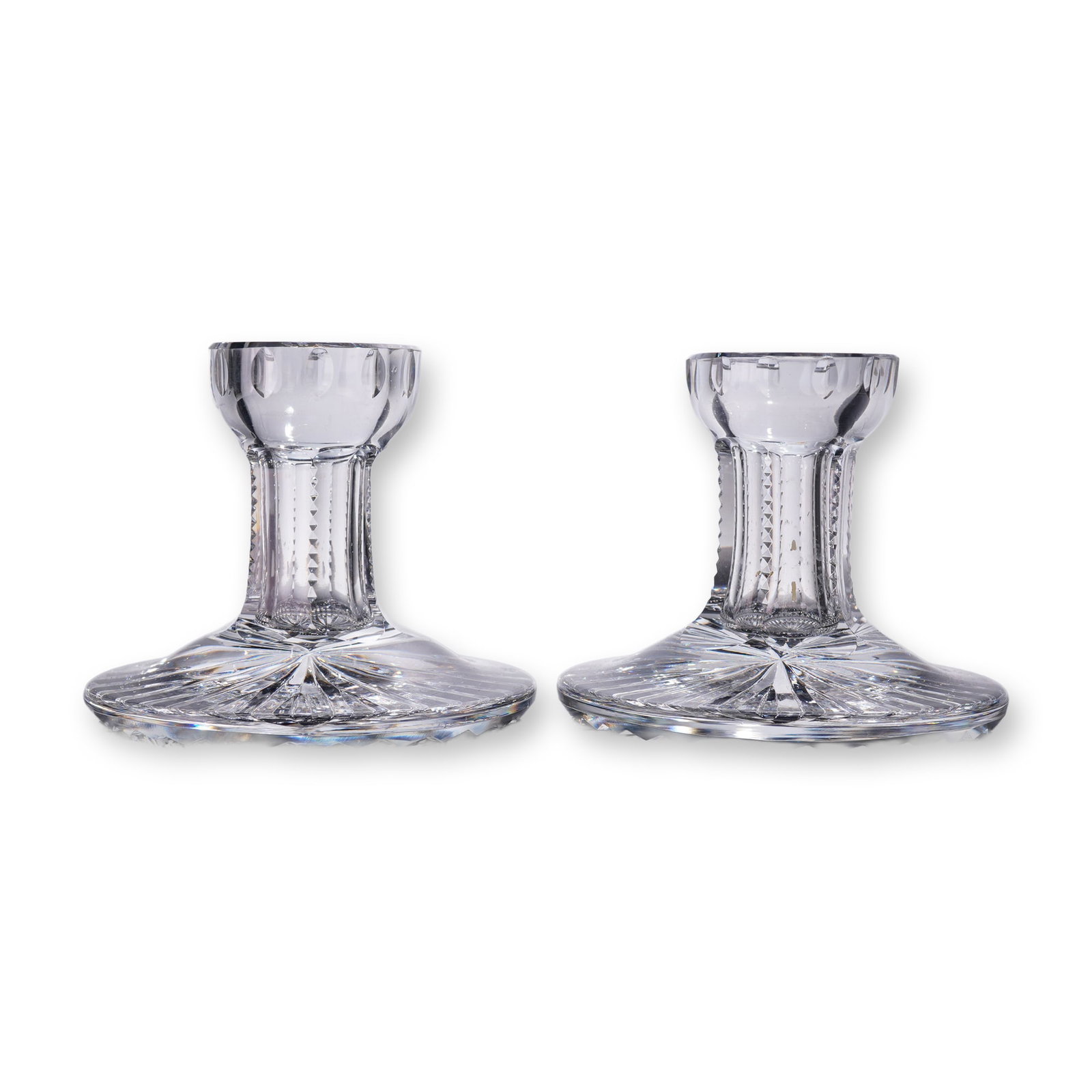 2pc Cut Crystal Candlesticks with Starburst Bases: Pair of cut crystal candlesticks featuring flared, scalloped rims and faceted stems with vertical diamond cuts, leading to broad circular bases with striking starburst patterns. The clear crystal catc