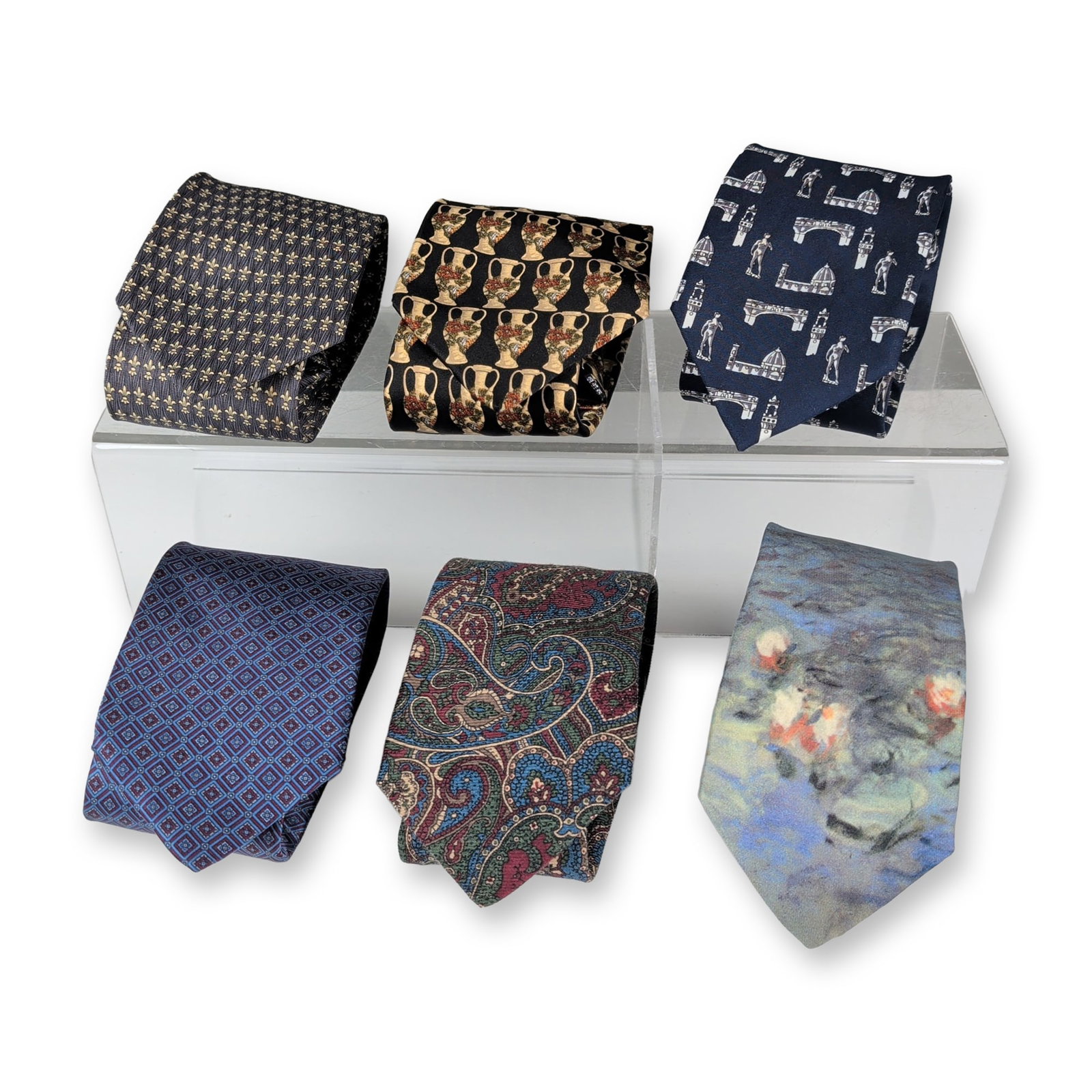 6pc Group of Designer Silk and Silk-Wool Neckties: Group of six men's neckties in silk and silk-wool blends, comprising assorted patterns and makers. Includes a charcoal gray silk tie with gold-tone fleur-de-lis motif, labeled Firenze and 100% silk; a