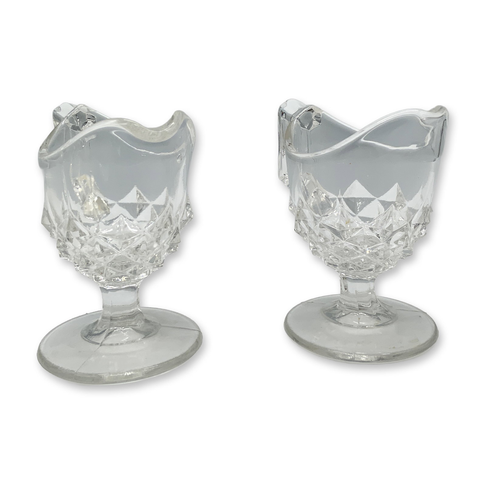 Pair of Art Glass Children's Creamer Jugs: Adorable duo of sawtooth variation clear glass jugs with handles and footing. Dimensions: 3.25"L x 2"W x 3"H Date or Era: 20th century