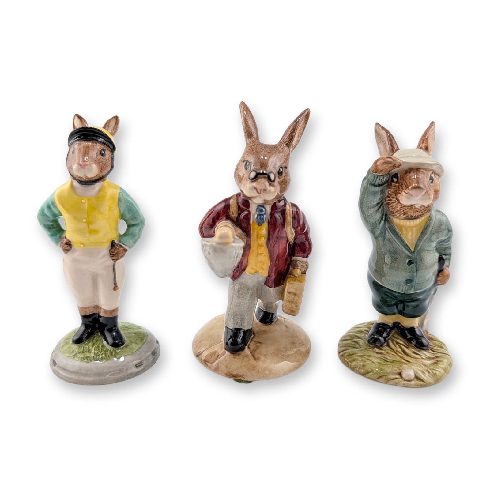 Three Royal Doulton Bunnykins Ceramic Figurines - DB32, DB84 & DB169: Royal Doulton glazed ceramic figurines from the Bunnykins series, featuring three rabbits in sporting and occupational attire. The group includes a jockey in yellow and green silks, a fisherman in a b