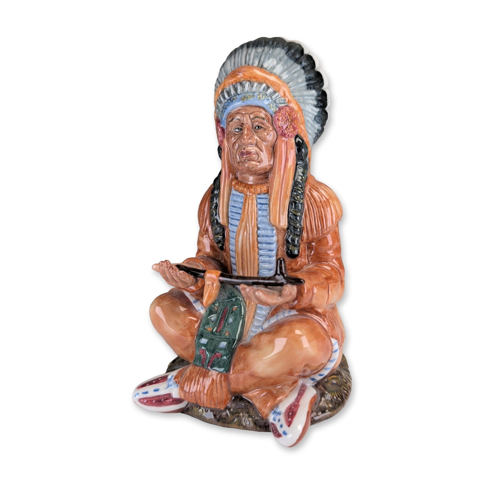 Royal Doulton The Chief Porcelain Figurine HN 2892: Royal Doulton The Chief figurine in polychrome glazed porcelain, featuring a seated Native American figure in traditional regalia. The figure is portrayed cross-legged on a rocky-textured base, wearin