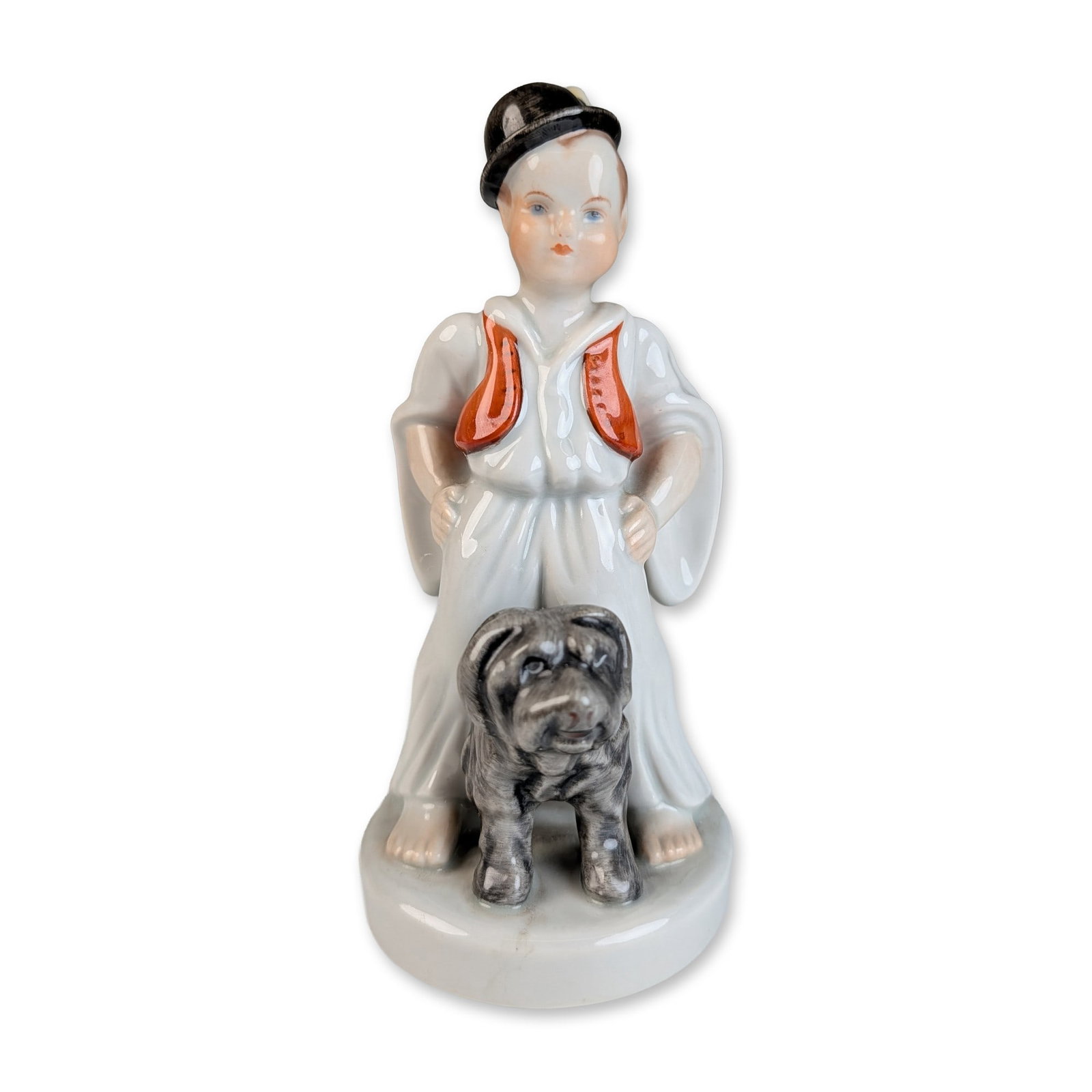 Herend Hungarian Porcelain Boy with Dog Figurine: Herend porcelain figurine depicting a young boy in traditional Hungarian folk attire, including a black bowler-style hat, white trousers, and a sleeveless red-orange vest. The boy stands over a