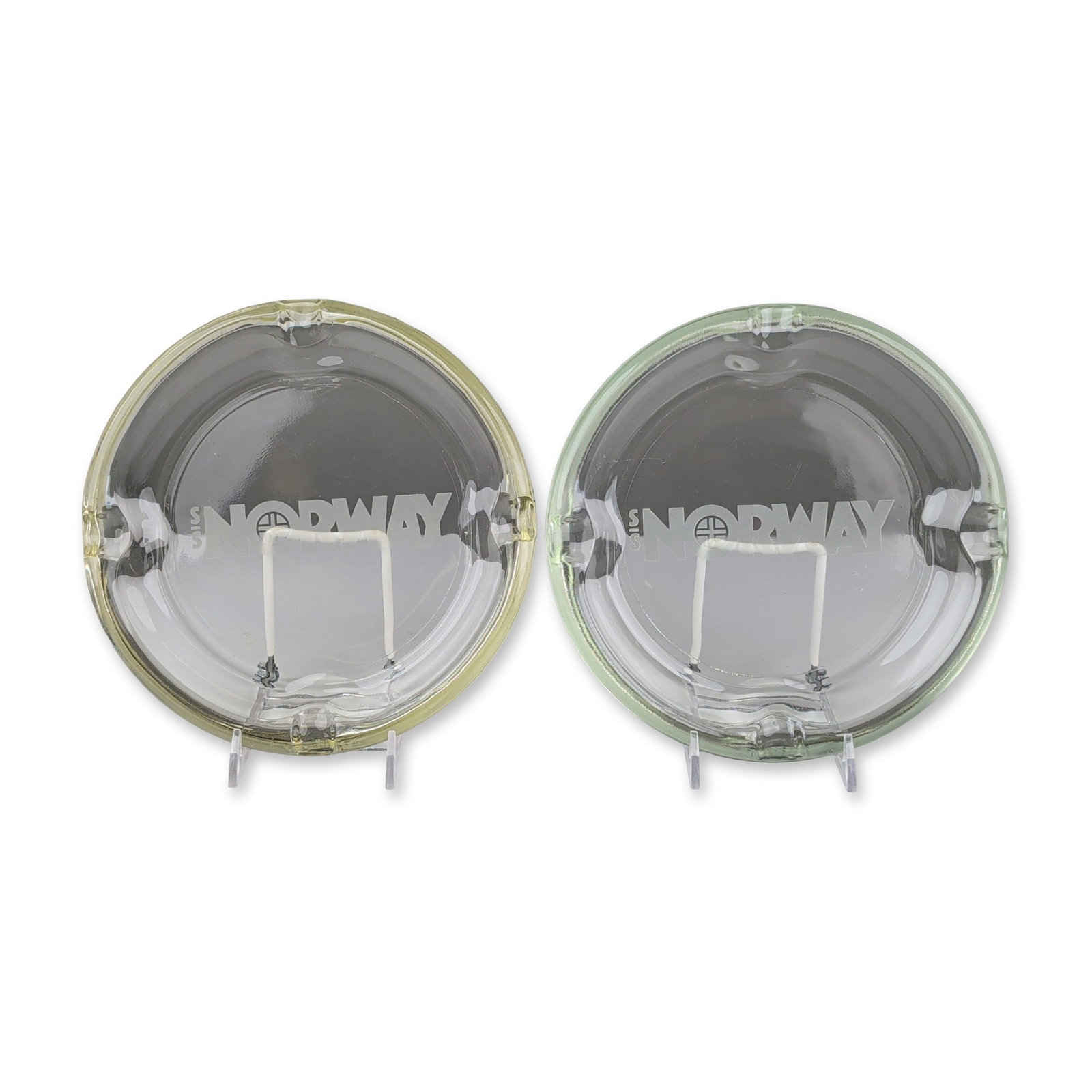 2pc Vintage S/S Norway Ocean Line Glass Ashtrays: A set of two S/S Norway cruise ship memorabilia ashtrays in pressed glass. Each circular piece features four cigarette rests. The underside of each ashtray is acid-etched with a logo consisting of a c