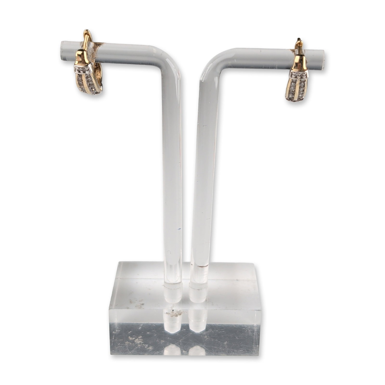 10K Two Tone Gold and Diamond Huggie Earrings: A pair of small two-tone gold huggie earrings featuring a wide, curved-front design. Each earrings features white gold accents and is set with two parallel rows of round brilliant-cut diamonds. The pr