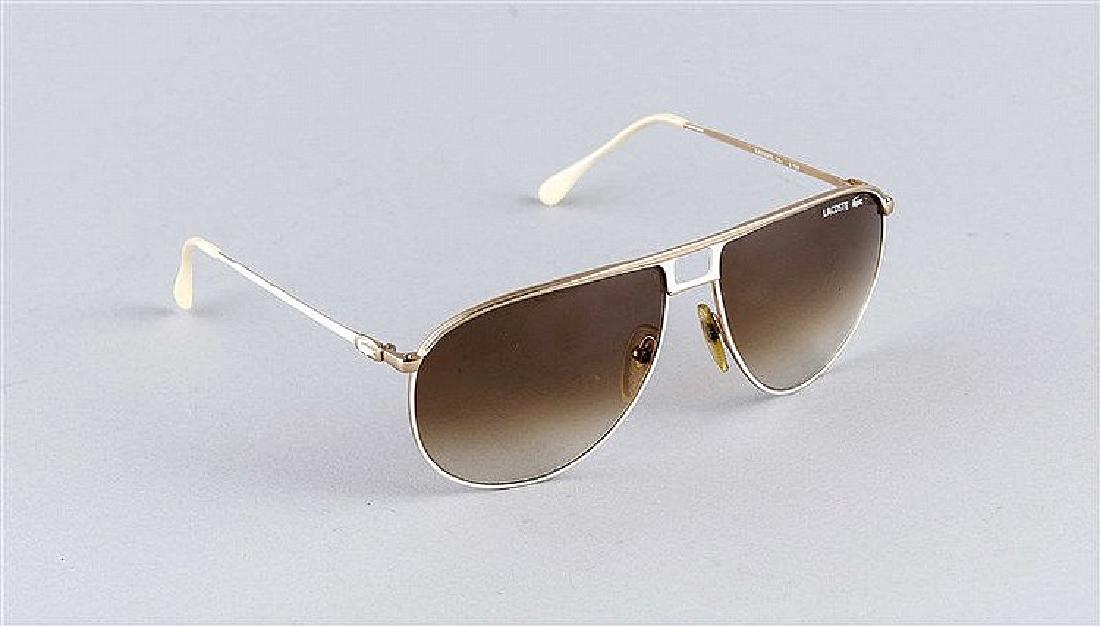 Lacoste Sonnenbrille, weißlackiertes und goldfarbener: Lacoste Sonnenbrille, weißlackiertes und goldfarbener Metallrahmen mit perlmuttfarbenen Kunststoffbügel, braun/grün getönte Gläser im Farbverlauf, kl. Gebrauchsspuren, L. ca. 15 cm. Notes: Sammle