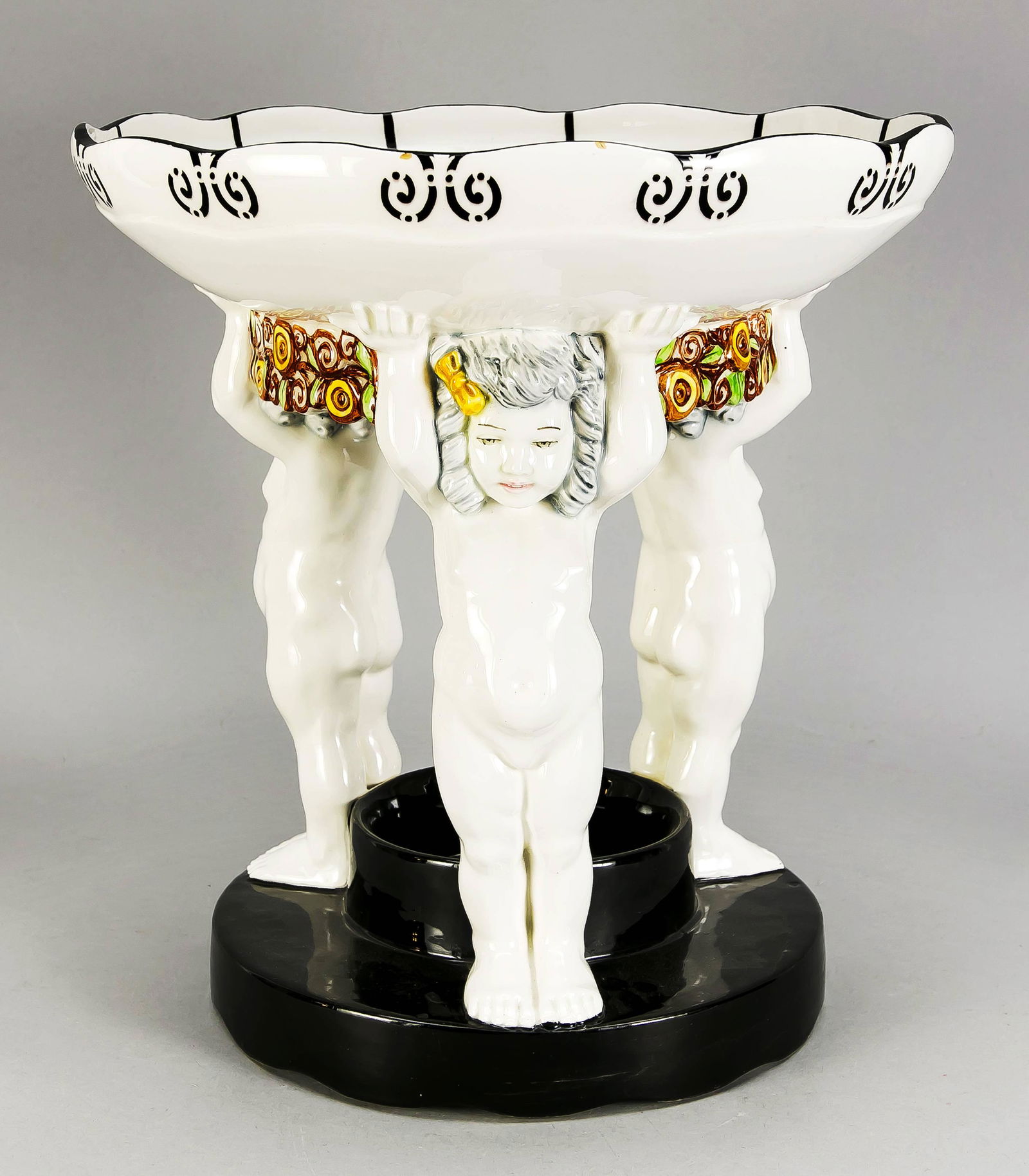 Large Art Nouveau bowl, Bohemi: Large Art Nouveau bowl, Bohemia, around 1900, probably Carl Klimt (1867-1945), three putti with raised hands carrying a round bowl, connected by flower garlands, polychrome painted, on a round foot in