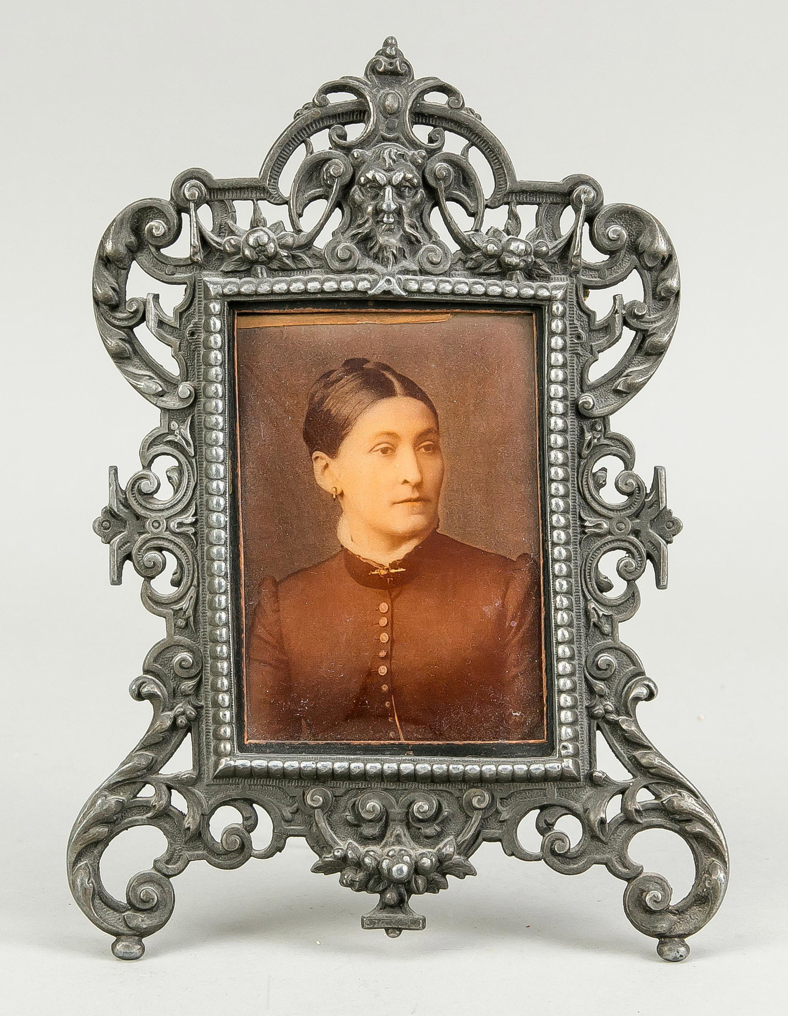 Historism picture frame, late 19th: Historism picture frame, late 19th century, cast metal. Renaissance style as scrollwork cartouche with mascaron, openwork, slightly warped. With old picture of a woman behind glass, h. 28 cm.