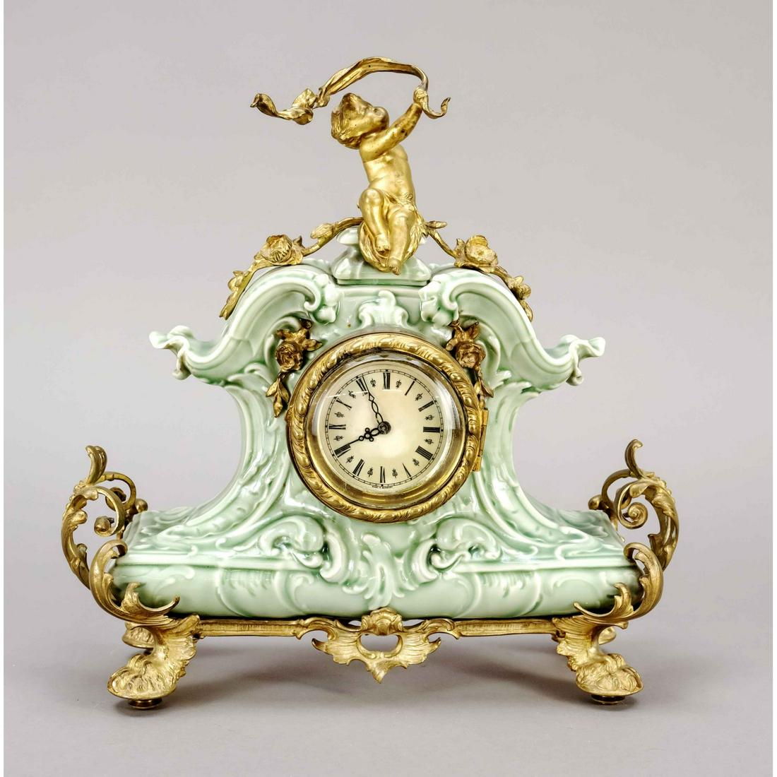 Kamin Uhr Seeger KPM, c. 1890,: Kamin Uhr Seeger KPM, c. 1890, greenish porcelain case decorated with rocailles, gilded bronze frame with rocailles, on paw feet, crowned by a putto swinging a ribbon, small round movement, paper cloc