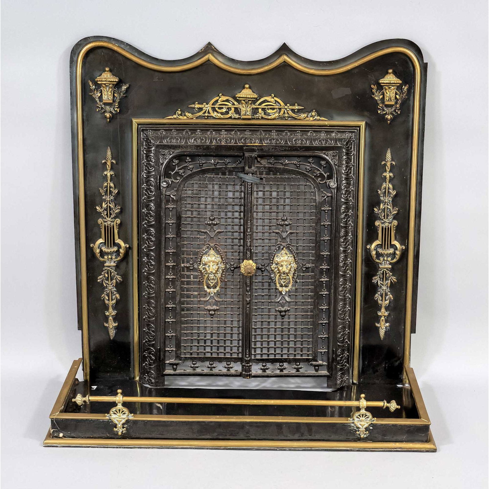 Fireplace porch, late 19th century: Fireplace porch, late 19th century, iron lacquered & brass. Fitted curved front with classicistic ornamental applications, lattice wing door with lion head mascarons with rings in the mouth. Matching 