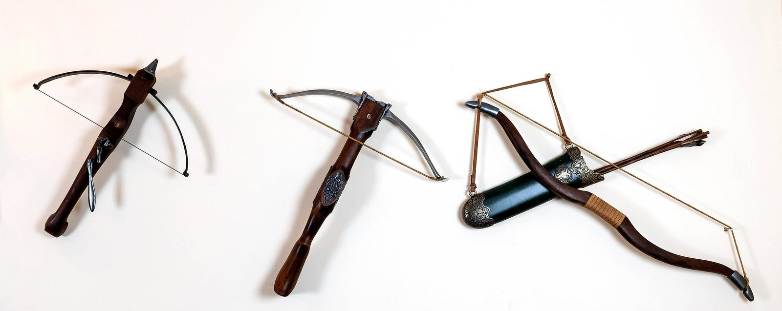 Group of three decorative weapons,: Group of three decorative weapons, 20th century, bow and quiver with fletched wooden arrows, 2 crossbows (1x damaged ), beech, metal applications, 50 x 45-57 x 50 cm, bow 90 x 40 cm. The preview of th