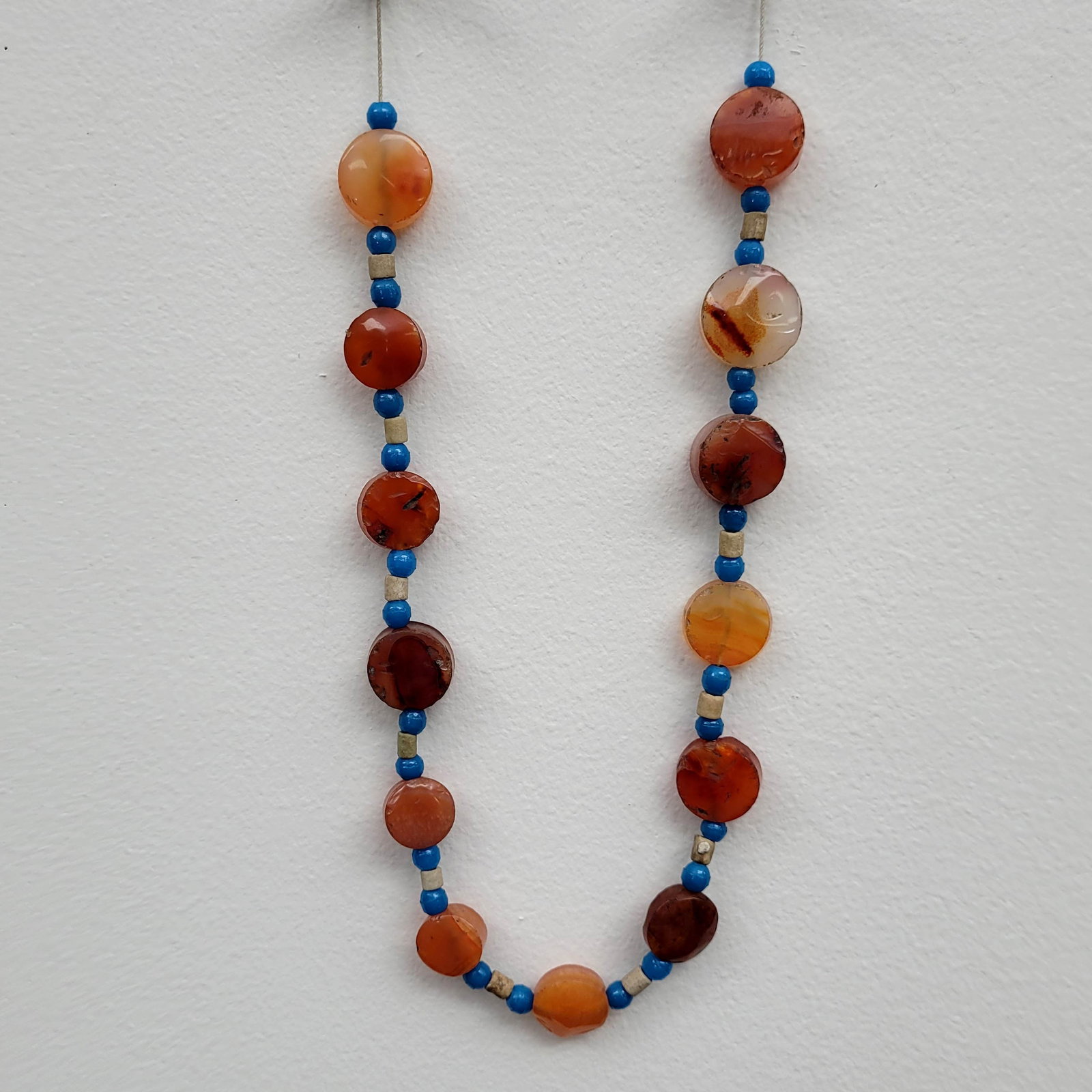 Mesopotamian Carnelian, Glass, and Faience Beaded Necklace: Mesopotamian beaded necklace. Beads made from orange carnelian, blue glass, and off-white faience. Circa 1500 to 1000 BC. Dimensions: 8 inches.
