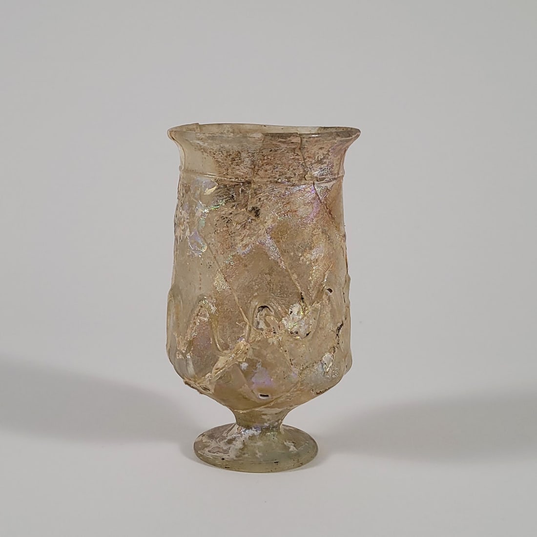 Roman Footed Glass Cup: Roman cream footed glass cup. Applied glass on the exterior. Repaired. 4th-7th century AD. Dimensions: 2 3/4 x 5 inches.