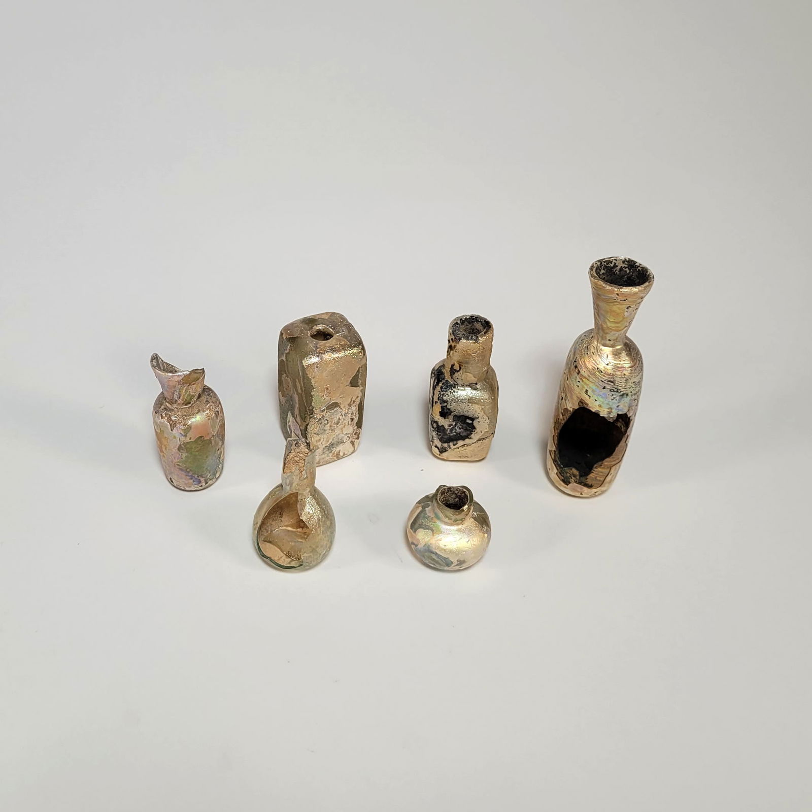 Lot of Six Roman Glass Vessels: Lot of six Roman glass vessels. The pale green glass vessels are comprised of one intact small jar and five fragmentary bottles. All highly iridescent. Dimensions: 3 inches (tallest).Provenance: Acqui