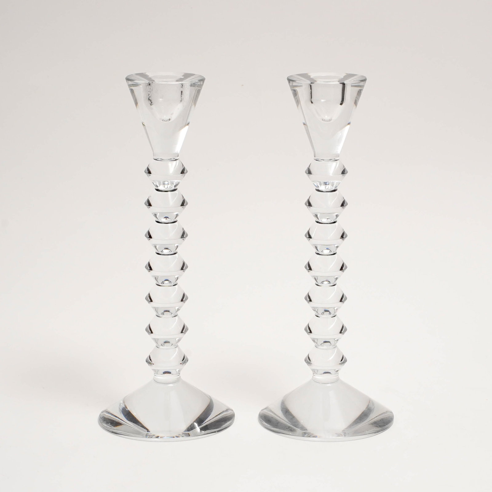 Pair of Baccarat Crystal Candlesticks: Pair of Baccarat clear crystal candlesticks, each with faceted socket, stacked geometric knop stem, and circular faceted foot. Marked Baccarat. H: 10 3/4 D: 4 in.