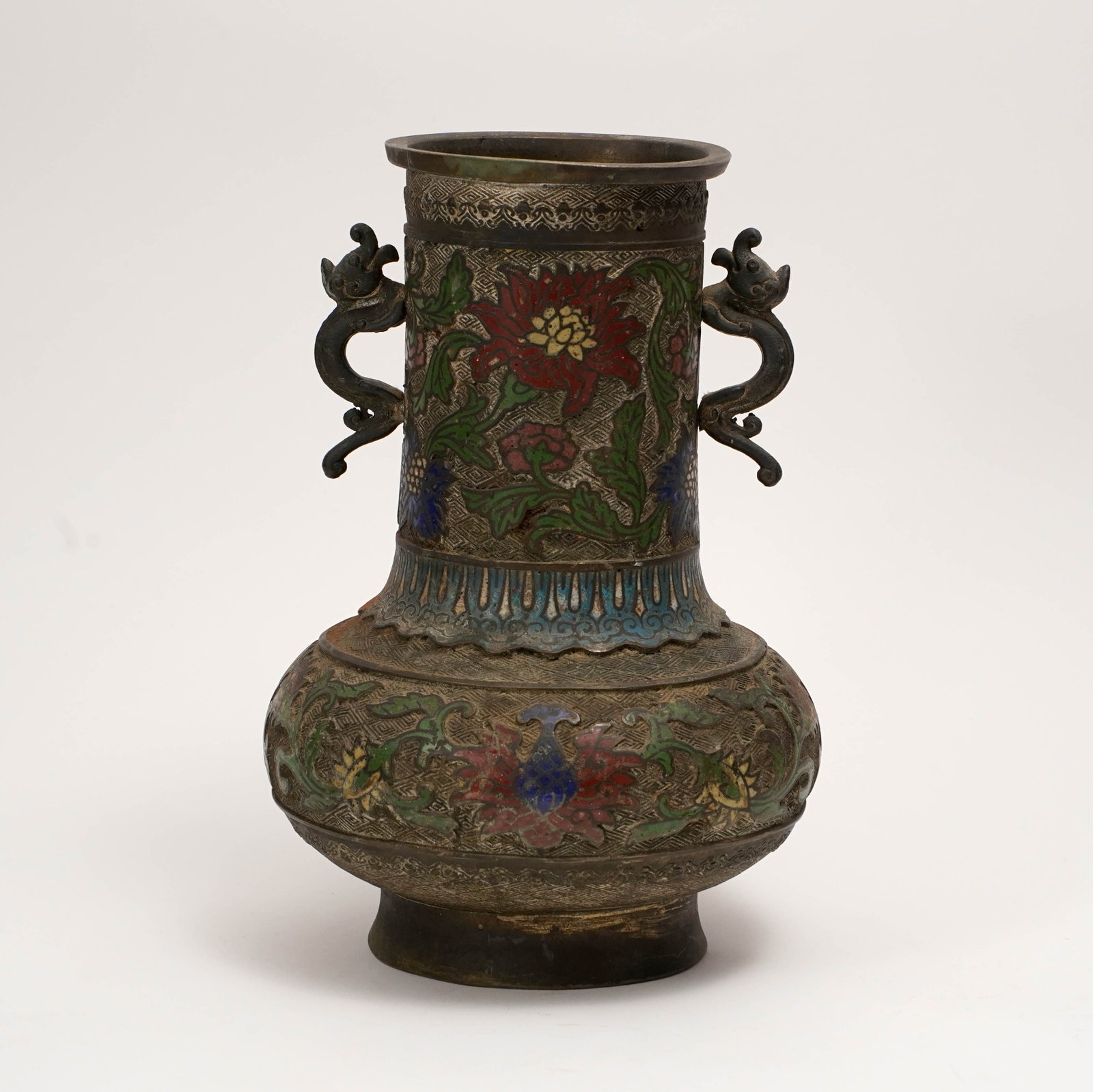 Chinese Cloisonné Enamel Vase: Chinese cloisonné enamel vase of baluster form, with twin dragon-form handles, decorated with large floral blossoms and scrolling foliage on a dark ground, with patterned borders and blue enamel