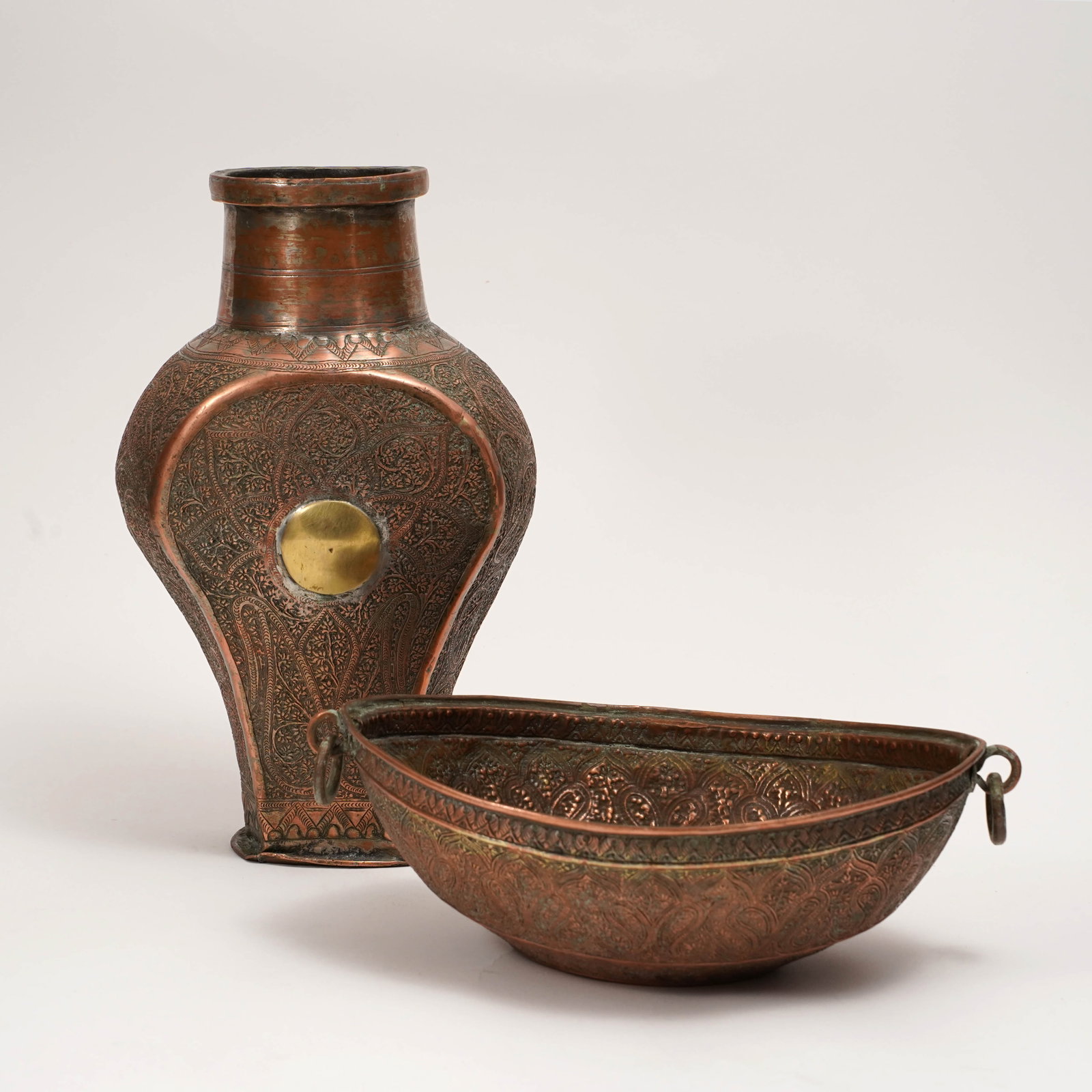 Indo-Persian Engraved Copper Vessel and Kashkul Bowl: Two Indo-Persian engraved copper vessels, comprising a flattened flask-form vessel with flared neck, arched raised front panel, brass circular boss, and dense engraved floral and foliate decoration;