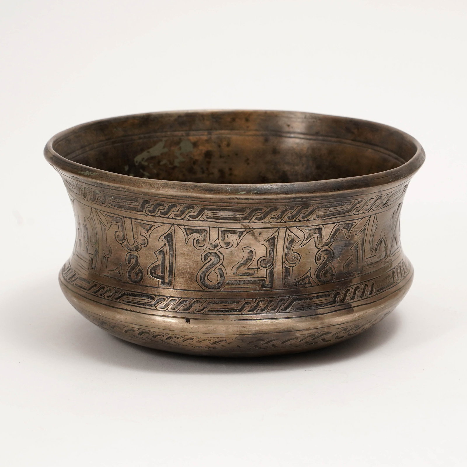 Islamic Engraved Brass Calligraphic Bowl: Islamic engraved brass bowl of rounded cylindrical form with flared rim, decorated with a broad band of stylized Arabic calligraphy between narrow geometric and scrolling borders. The surface has an