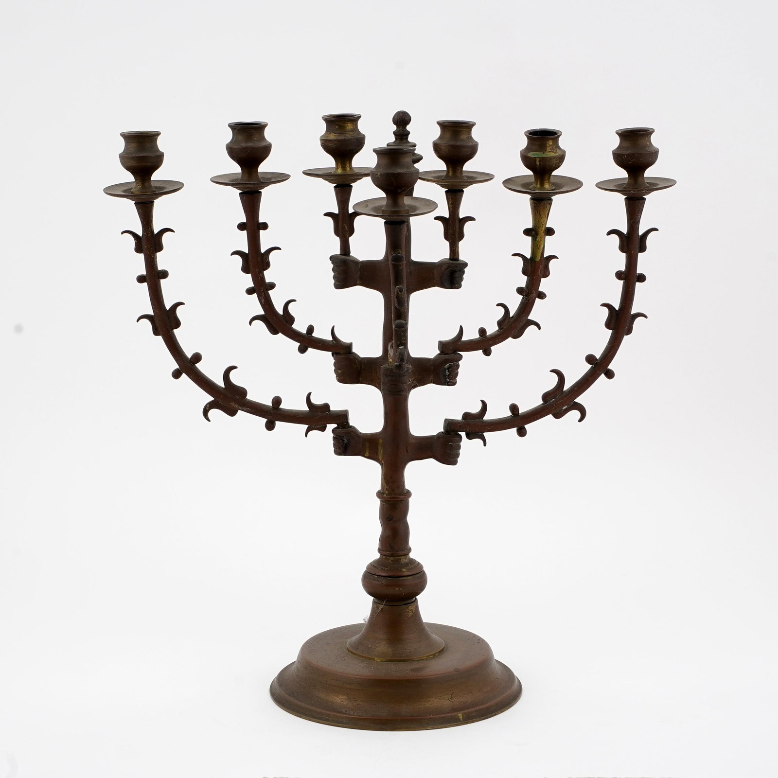 Seven-Light Brass Menorah Candelabrum: Brass or bronze seven-light menorah-form candelabrum, with central stem and six scrolling side branches, each fitted with candle cups and drip pans. The branches decorated with applied foliate or thor