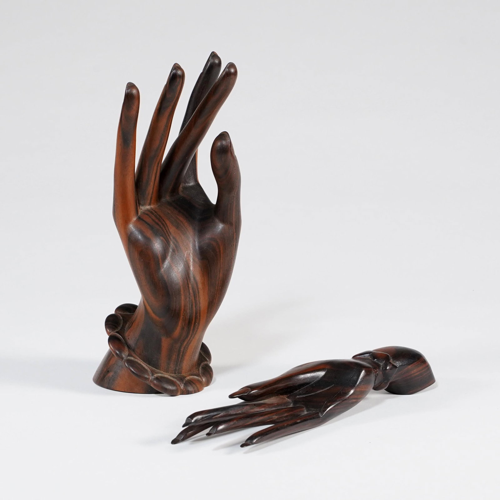 Lot of Two Carved Wood Hand Sculptures: Pair of carved wood decorative hand sculptures, one modeled upright with open palm and bracelet-form wrist, the other reclining with extended fingers. Each in dark polished wood with visible grain