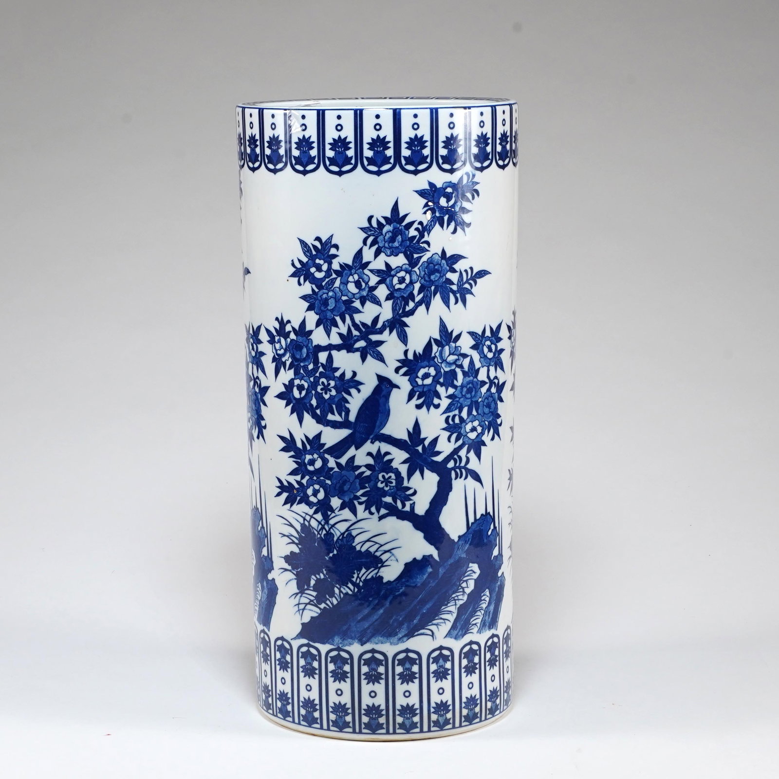 Chinese Blue and White Porcelain Cylindrical Vase / Umbrella Stand: A Chinese blue and white porcelain cylindrical vase or umbrella stand, decorated with a continuous garden scene of flowering branches, rockwork, birds, and foliage. The upper and lower borders are