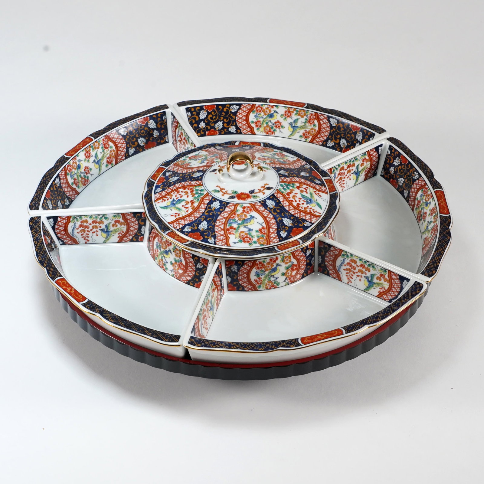 Japanese Imari Porcelain Lazy Susan Serving Set: Japanese Imari-style porcelain lazy Susan serving set, with sectional fan-form dishes and central covered bowl, decorated with floral and bird panels in cobalt, iron red, green, and gilt, on black