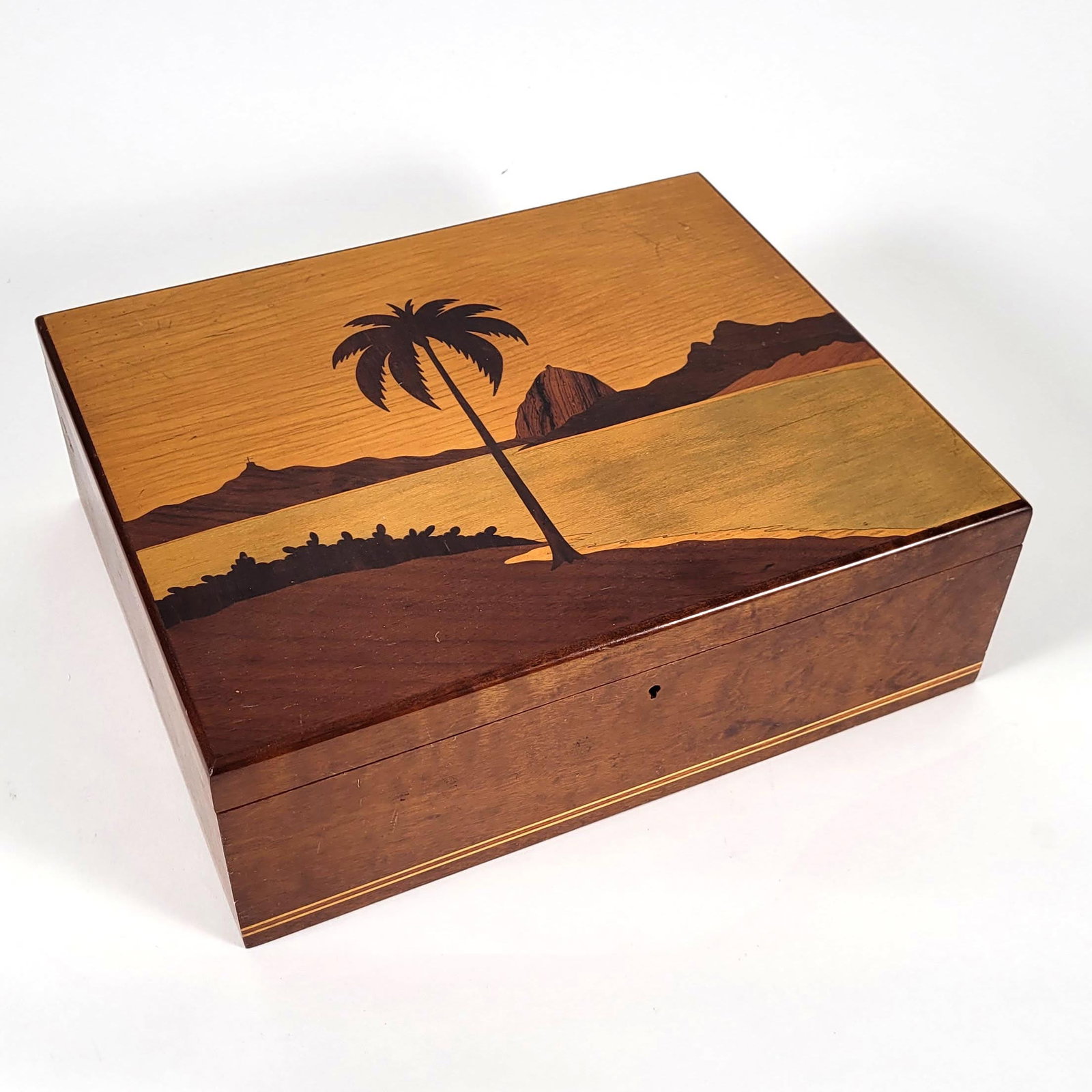 Egyptian Marquetry Wood Box: Egyptian rectangular wood box with hinged lid, decorated with inlaid marquetry scene of a palm tree, water, and desert hills or pyramidal forms in contrasting wood tones. The case with polished