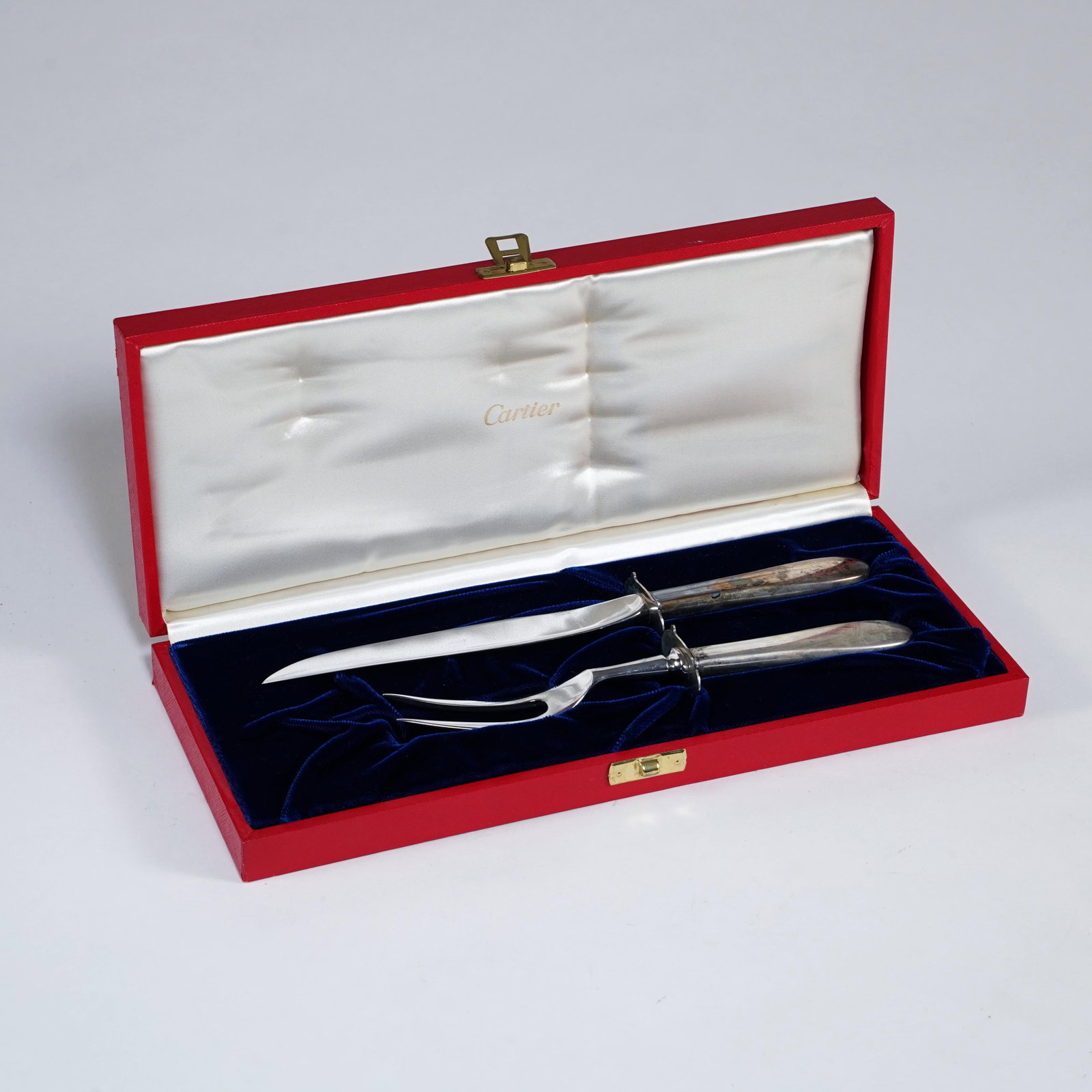 Cartier Sterling Silver Handled Carving Set: A Cartier two-piece carving set comprising a carving knife and carving fork, each with sterling silver handles and polished steel blade/tines. Presented in a fitted red Cartier case with blue velvet
