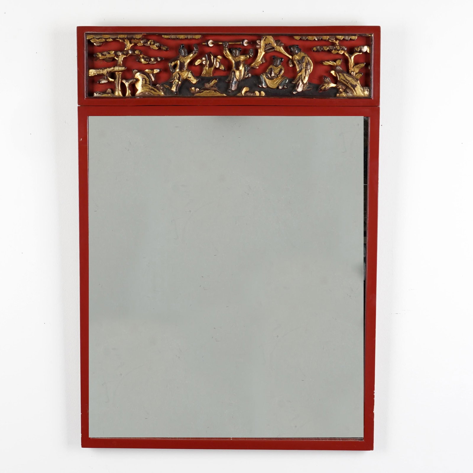 Chinese Red Lacquer Mirror with Gilt Figural Panel: A Chinese decorative wall mirror with red lacquered rectangular frame, the upper frieze inset with a gilt and black relief panel depicting figures in a landscape with trees, rocks, and pavilion-style 