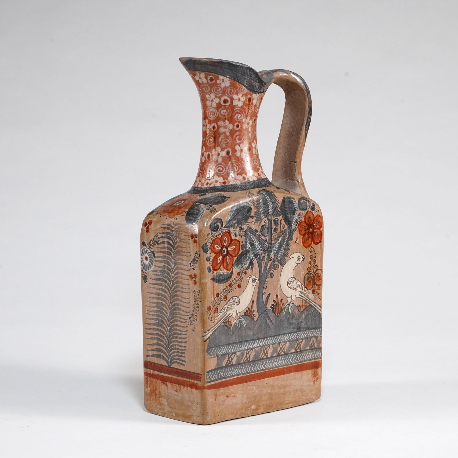 Latin American Painted Pottery Pitcher / Ewer: A hand-painted pottery pitcher of rectangular bottle form, with a tall flared spout, applied loop handle, and flat-sided body. The front is decorated with a folk-art landscape scene of birds among