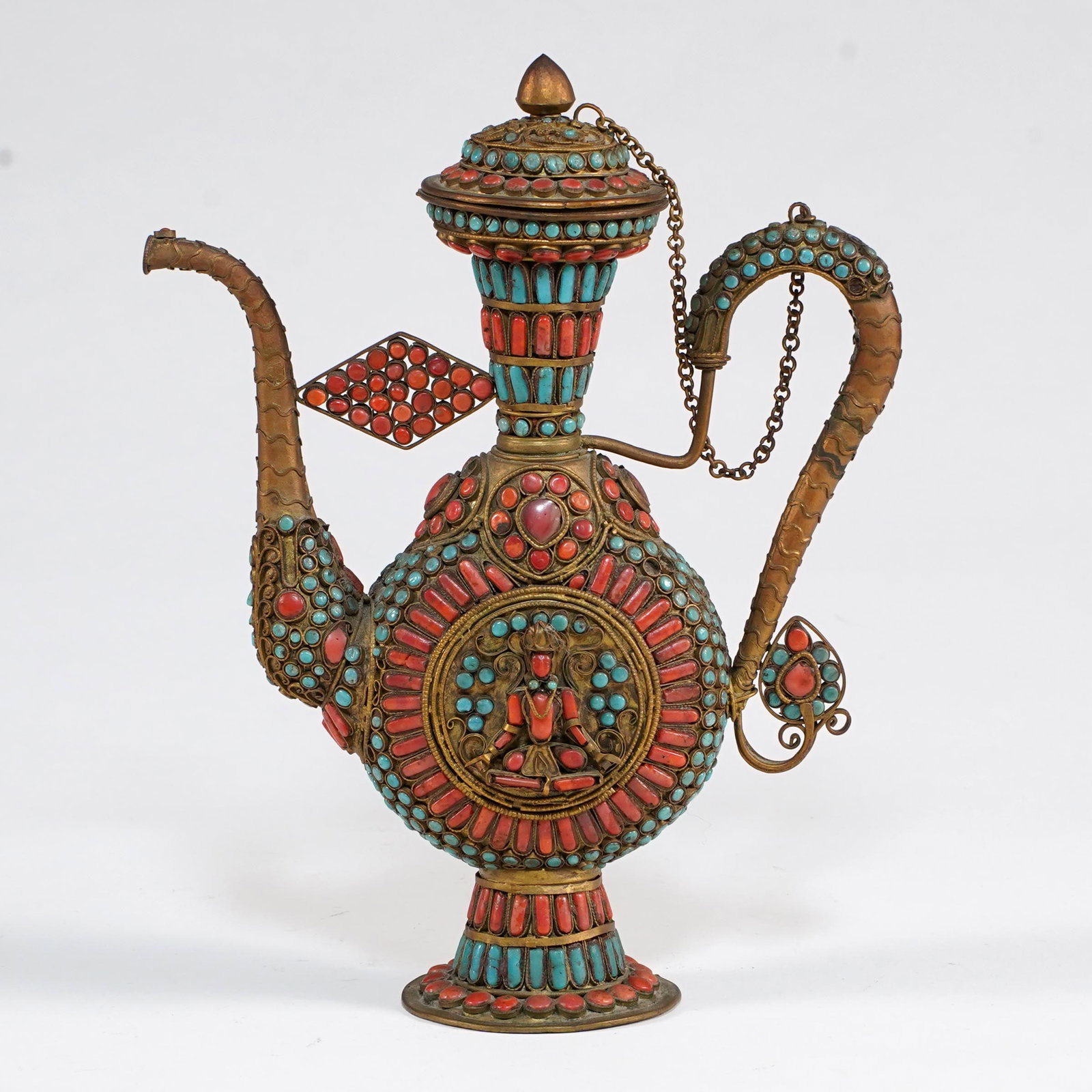 Tibetan/Nepalese Jeweled Metal Ewer: Tibetan/Nepalese style jeweled metal ewer, brass or copper alloy, decorated throughout with applied turquoise and coral, filigree mounts, and a central seated Buddhist figure medallion. The vessel