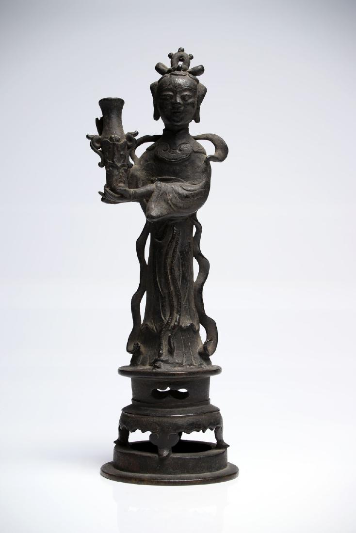 Woman with Vase: Bronze China 16th ct H: 29 cm A noble lady standing on a round platform in a long robe, a long scarf adorns her shoulders falling onto the ground. In her right hand she is holding a vase.