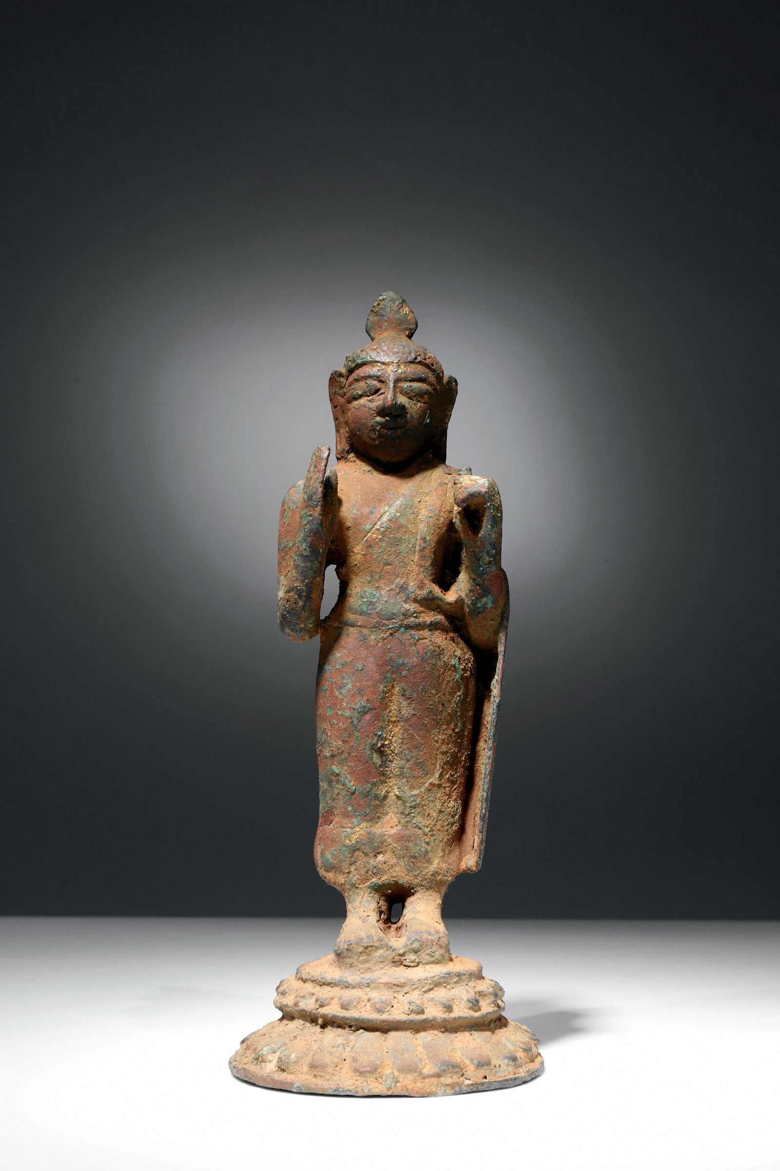 STANDING BUDDHA: Bronze with traces of gildingCeylon, 12th century or earlierDimensions: Height 16,5 cmWeight: 341 gramsBuddha standing on a circular base of larger and smaller lotus petals with rim. Both hands are ra
