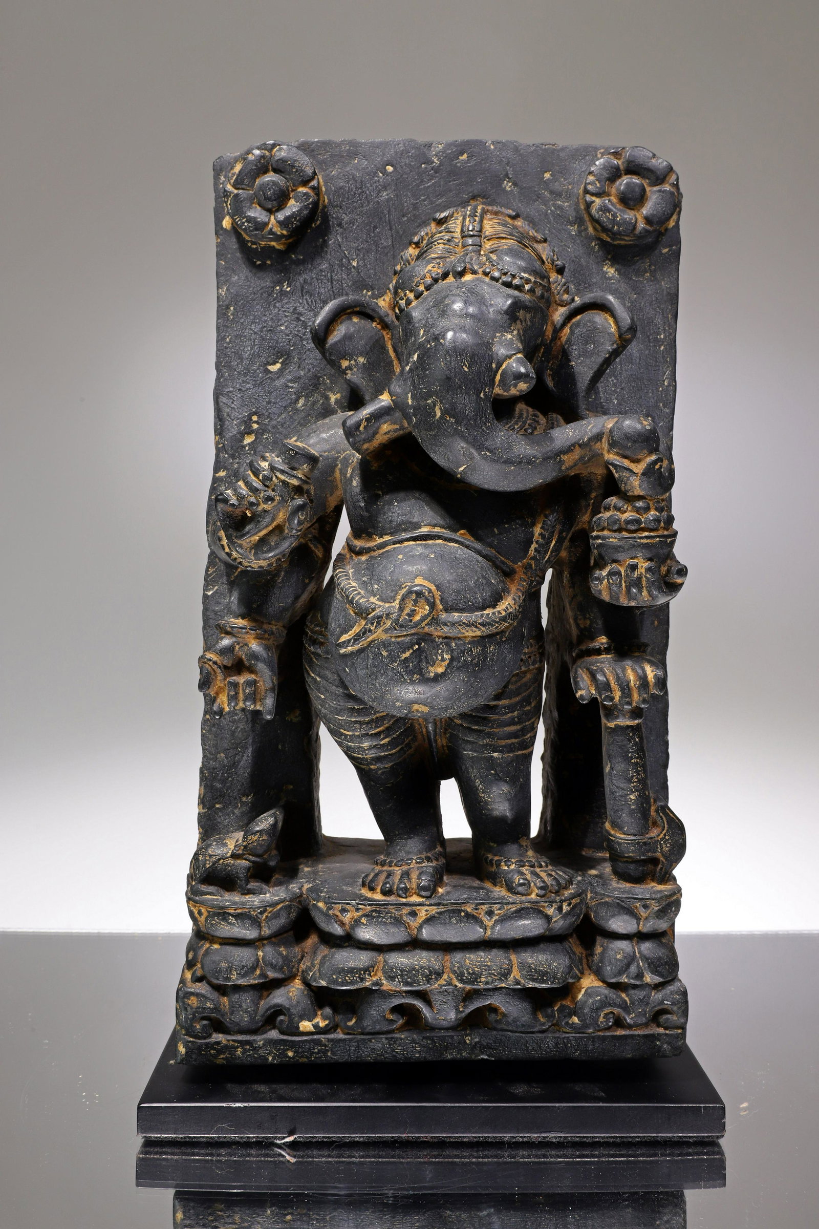STANDING GANESHA: Black StoneIndia , 18th century or earlierDimensions: Height 31 cm by 17 cm without baseWeight: 8662 grams with baseStone stele with a standing Ganesha in open work. The elephant king is standing on a
