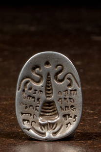 TSA TSA FORM DEPICTING A STUPA SILVER TIBET 17TH CENTURY: Dimensions: Height 2,8cm Wide 2,2 cm Depth 1,1 cm Weight: 12,1 grams This oval Tibetan seal amulet (tamga) is cast in silver and features a deeply incised design on the face, depicting a central stupa