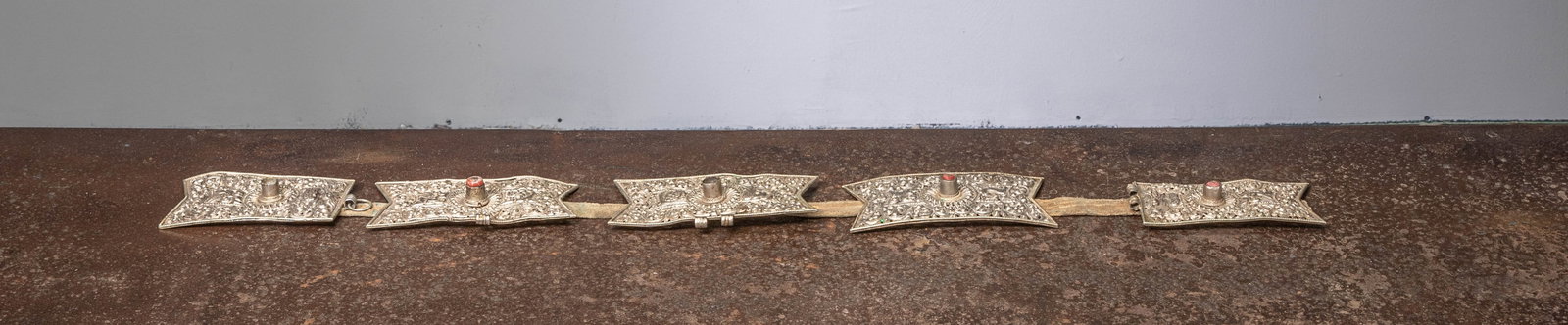 A WHITE METALL BELT, TIBET, 19TH CENTURY: Dimensions: Height 8,5 cm Wide 80 cm Depth 2 cmWeight: 497 grams Composed of a series of rectangular white metal plaques linked by leather straps, each plaque finely repoussé-worked with scrolling fo
