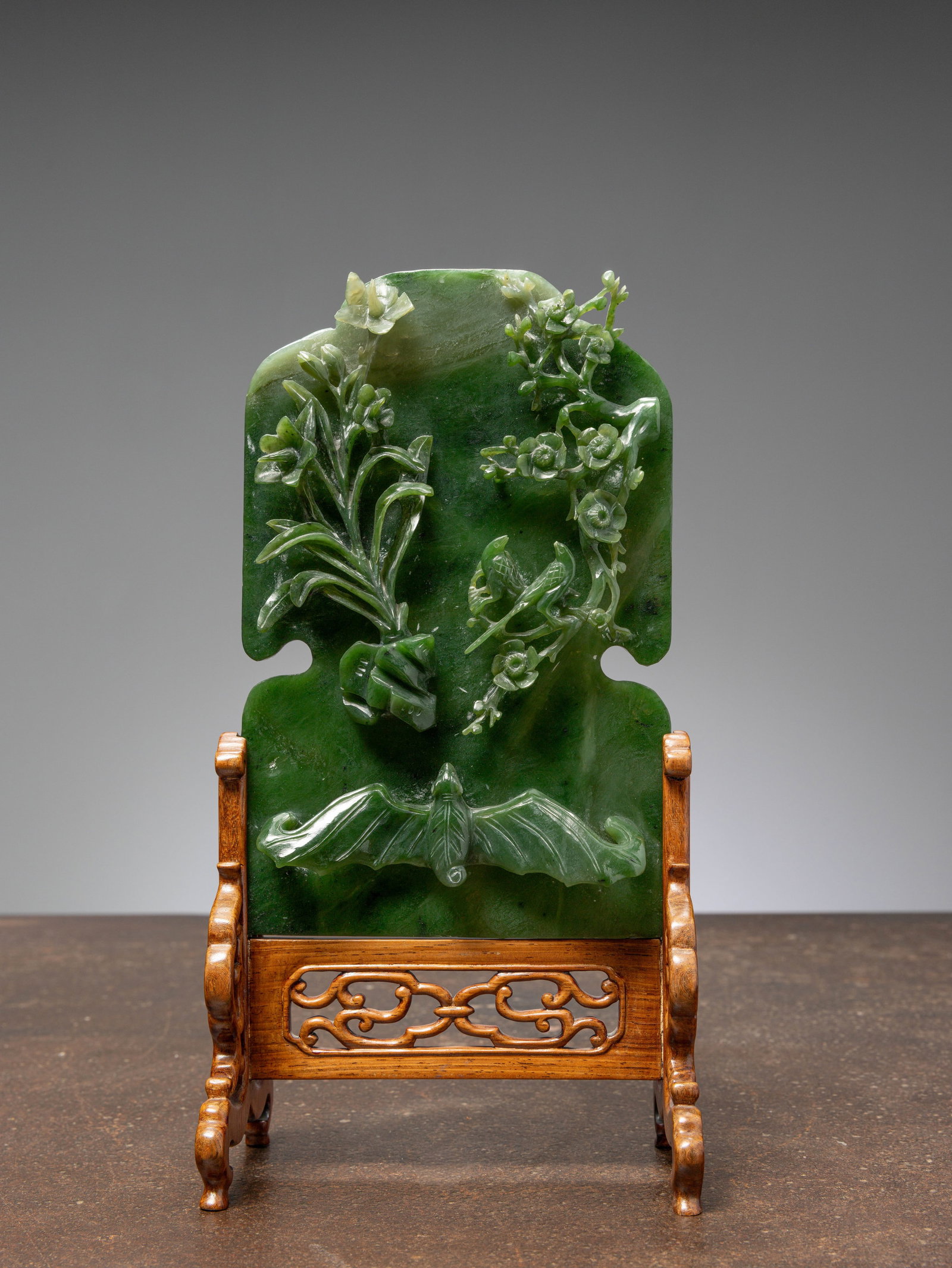 (R) A GREEN JADE SCREEN WITH BAT, FLOWERS, AND BIRDS, CHINA, QING DYNASTY (1644-1911): Dimensions: Height 30 cm Wide 15 cm Depth 9 cm Weight: 756 grams Carved from a rich, mottled green jade, this upright table screen is finely worked in high relief with auspicious motifs. On the
