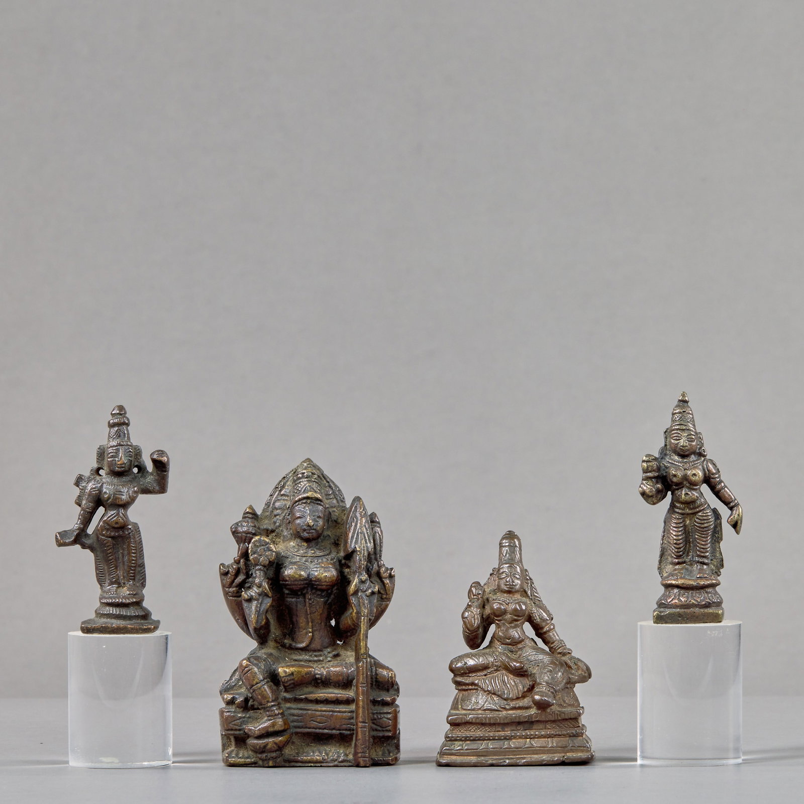 A GROUP OF FOUR INDIAN BRONZE DEITIES 17TH TO 18TH CENTURY: Dimensions: Height 8,8 cm Wide 5,2 cm Depth 2,5 cm Weight: 397 grams Comprising four bronze devotional figures, including a seated multi-armed deity holding attributes and a spear, a seated goddess in