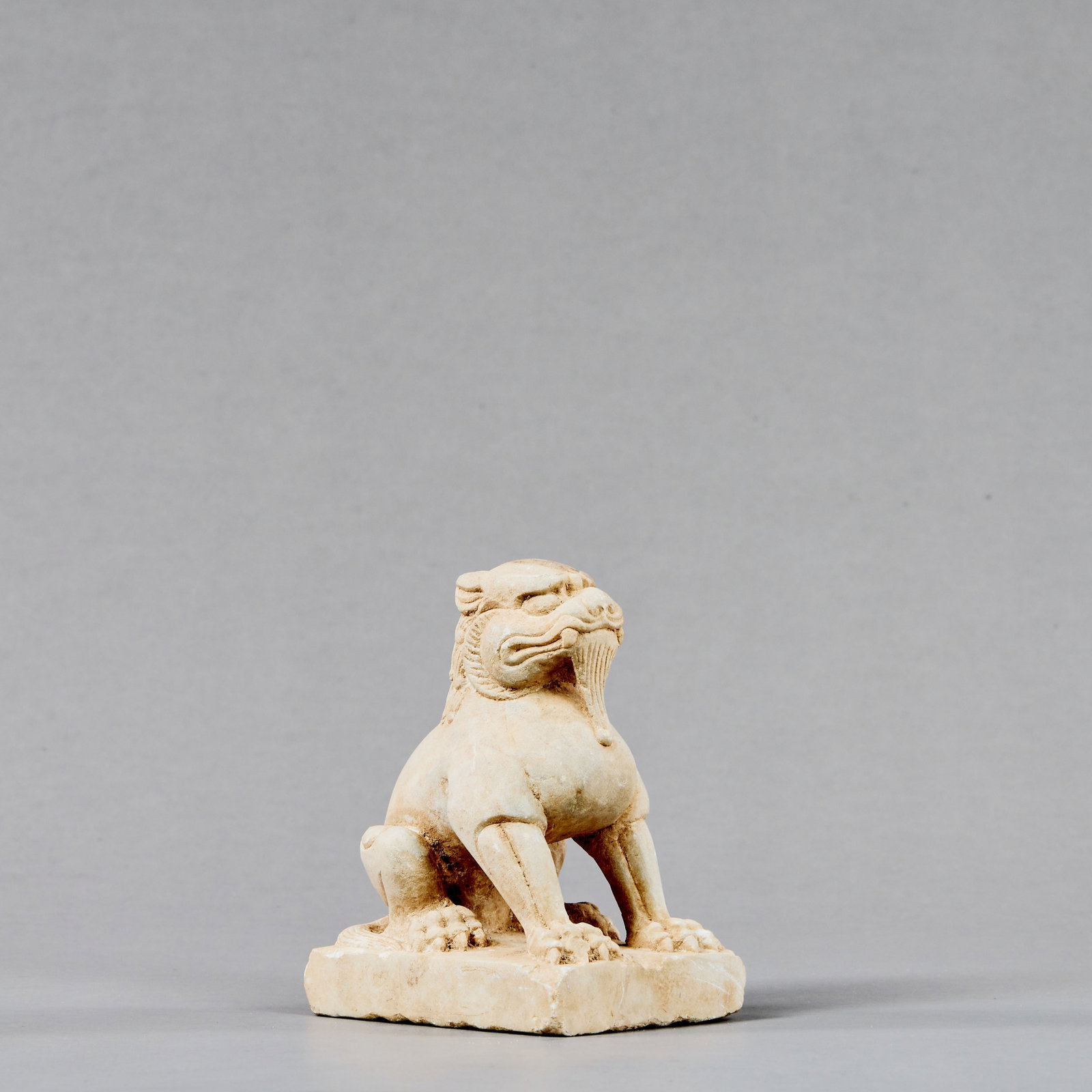 STONE GUARDIAN LION (ZHENMU SHOU), TANG DYNASTY: Dimensions: Height 10 cm Wide 6 cm Depth 8 cm Weight: 495 grams Carved in the round from a pale limestone, the guardian beast is shown seated upright on a rectangular plinth with its forelegs e