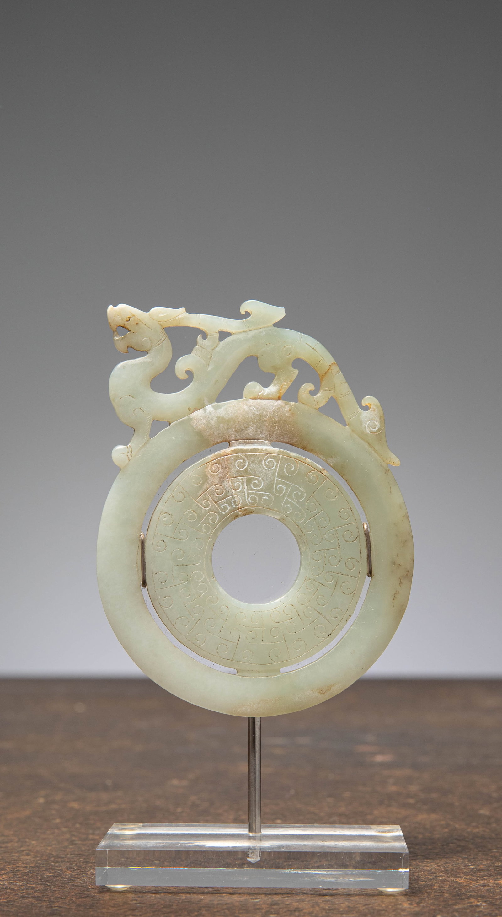 (R) A JADE BI DISC WITH CHILONG, LIGHT GREEN JADE, CHINA, 19TH CENTURY: Dimensions: Height 9,5 cm Wide 7 cm Depth 0,5 cm without base Weight: 100 grams with base Light green jade, carved as a circular bi disc with a central