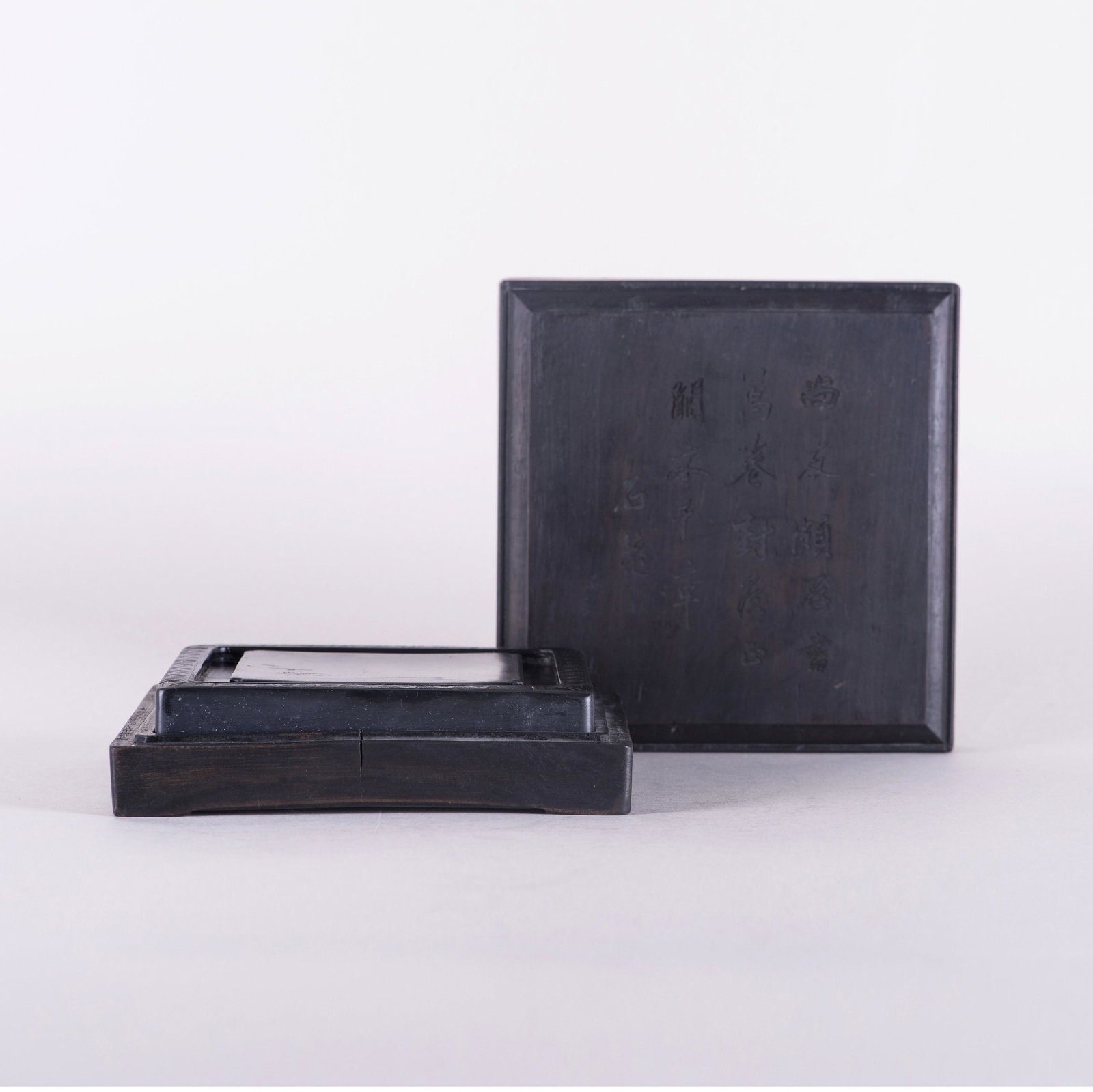 A CHINESE INKSTONE WITHIN A HARDWOOD BOX: A Chinese inkstone within a carved calligraphic hardwood box. L 6.5 xW 7 x H 6 cm