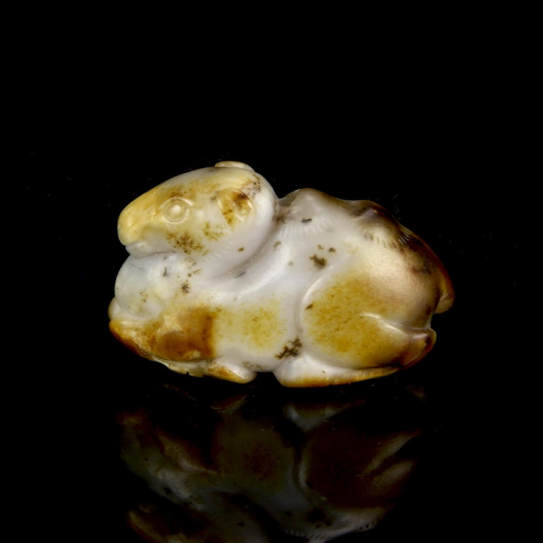 Celadon and Russet Jade Figure of a Camel: The pebble sensuously worked as a recumbent horse with legs neatly tucked beneath its body, the stone of a pale celadon tone with russet veins. Width 1 1/2 in., Height 1 in.