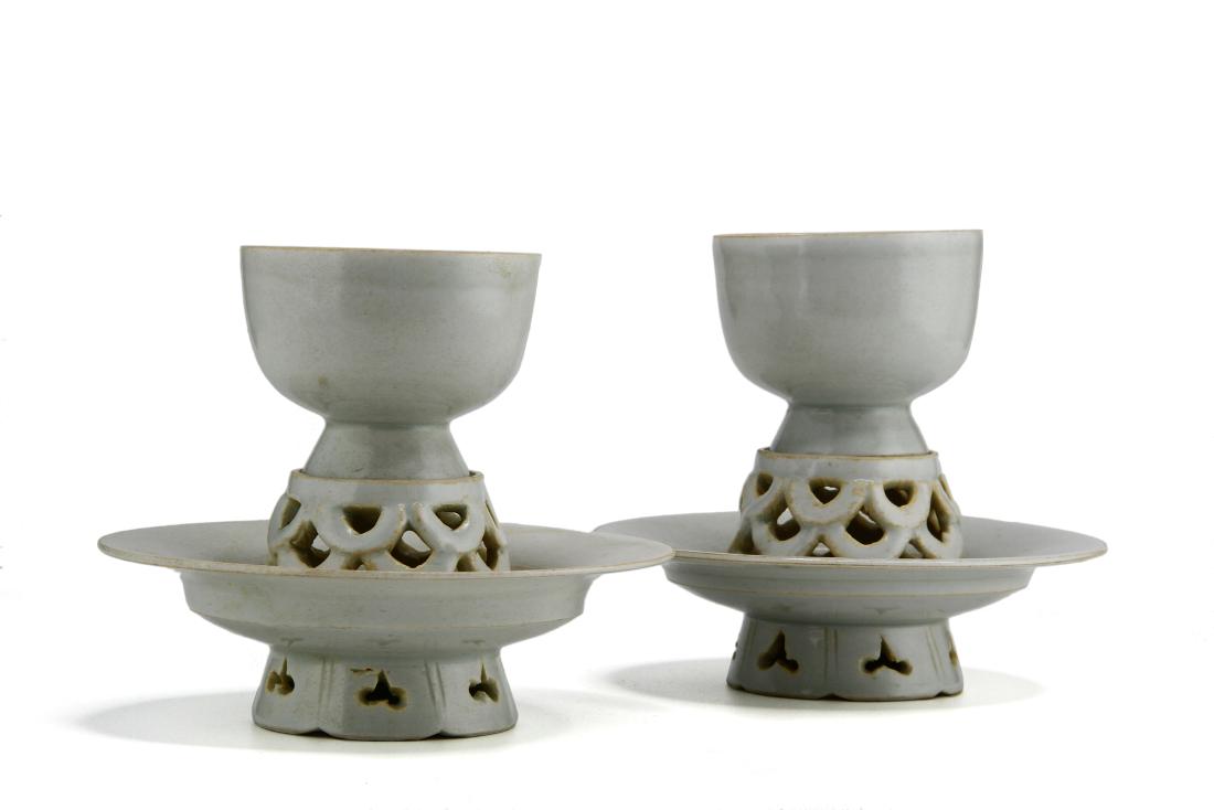 Pair Ying Ching Cupstands/Cups: Each cup resting on a stand with a pierced center pedestal and trefoil-pierced foot, applied with a bluish transparent glaze, the base and interior of the foot left unglaze revealing a white biscuit p