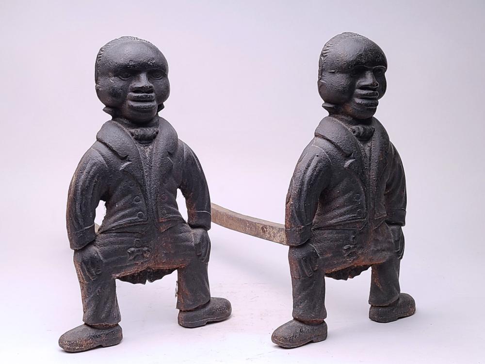 A set of andirons, circa 1900.: A set of andirons, circa 1900. Each of a black butler dressed in fancy top coat with hands on knees and knees bent. Both are painted black and are cast from one piece of iron with extended arm inserte