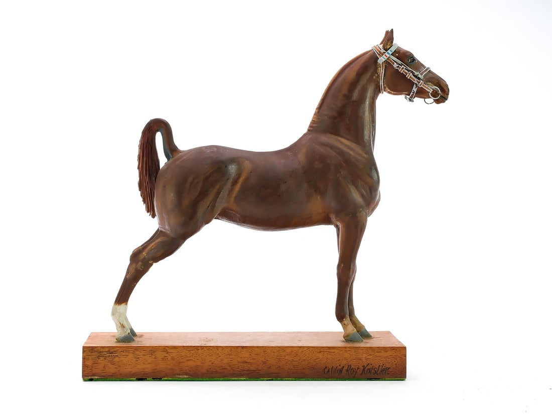 Calvin Kinstler (1890-1954): Carved model of a hunter horse. With applied wooden arched tail and painted metal bridle. Signed by the maker on one side of base. Sticker from Abercrombie & Fitch, New York on underside. Measures 9.5