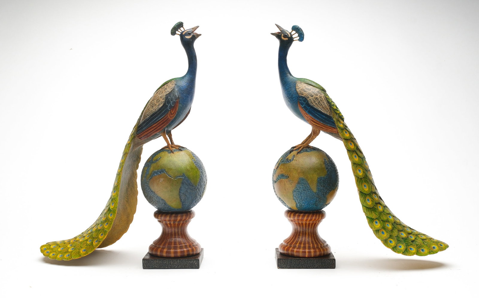 Frank Finney (b.1947), Cape Charles, Virginia.: Outstanding pair of peacocks on terrestrial globe bases. Up looking heads with open beaks and graceful tails. Relief feather carving. Measure 13.5" tall including base.
