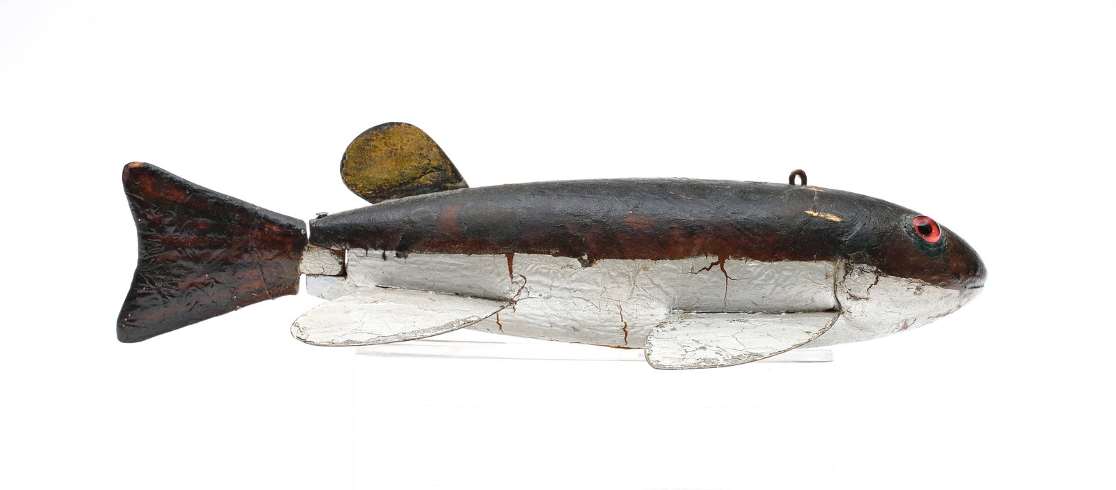 Alexander Yock Meldrum (1887-1971), Mt. Clemens, Michigan.: Early fish decoy with articulated tail. A catfish with red glass eyes, carved gills and mouth. Metal fins. Collection sticker on underside indicates it was in the Ron Swanson collection. 9"