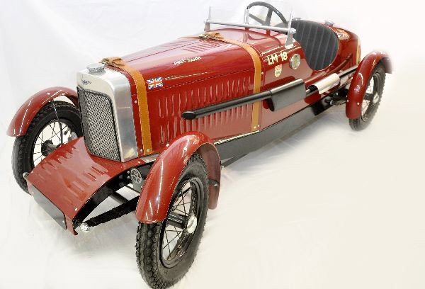 Pressed Steel Aston Martin Pedal Car: 74" long. Boat tail design, made by Stevenson Brothers. Handmade steel body, aluminum grille, leather seat & hood straps. Pneumatic rubber Schwalbe tires/spoke wheels, and full fender. Like new, C9