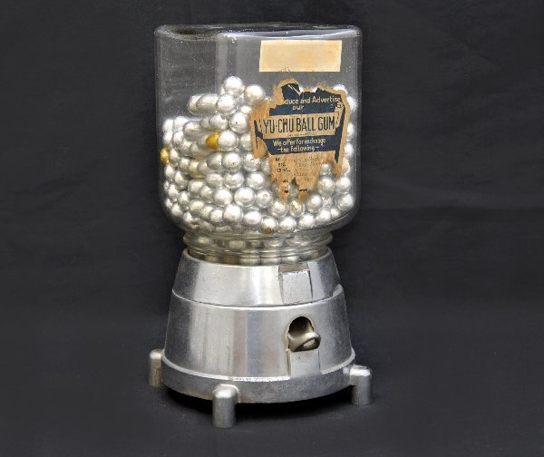 1925 Yu-Chu Gumball Machine: 7 X 7 X 12 1/2", chromed base, dated 1925. Glass top has worn, but mostly readable label. Functional. Contains chocolate balls (not for consumption).
