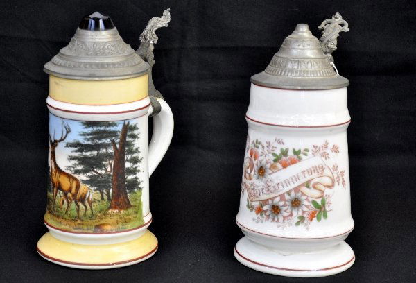 2 Vintage Steins with Ghost Bottoms: 8" Porcelain stein, decorated with "Fur Erinnerung"(In Memory Of). Bottoms up to light reveals an image of a woman & child ghost impression; second stein has Buck in forest motif with blue glass top w