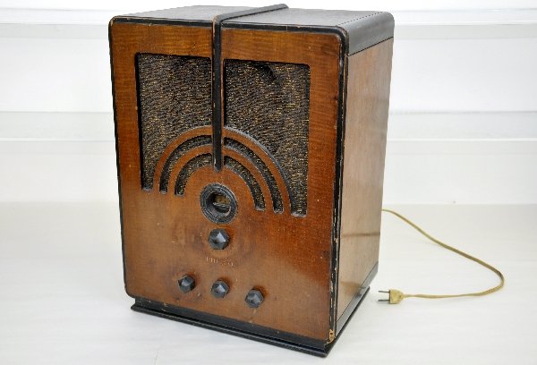 Art Deco Philco short wave Radio: 12 1/2 X 8 X 16 1/2". Walnut & mahogany case with Bakelite knobs. Turned on and light went on when plugged in. Speaker cloth has a small tear at top and the case shows signs of use & age. Examine phot
